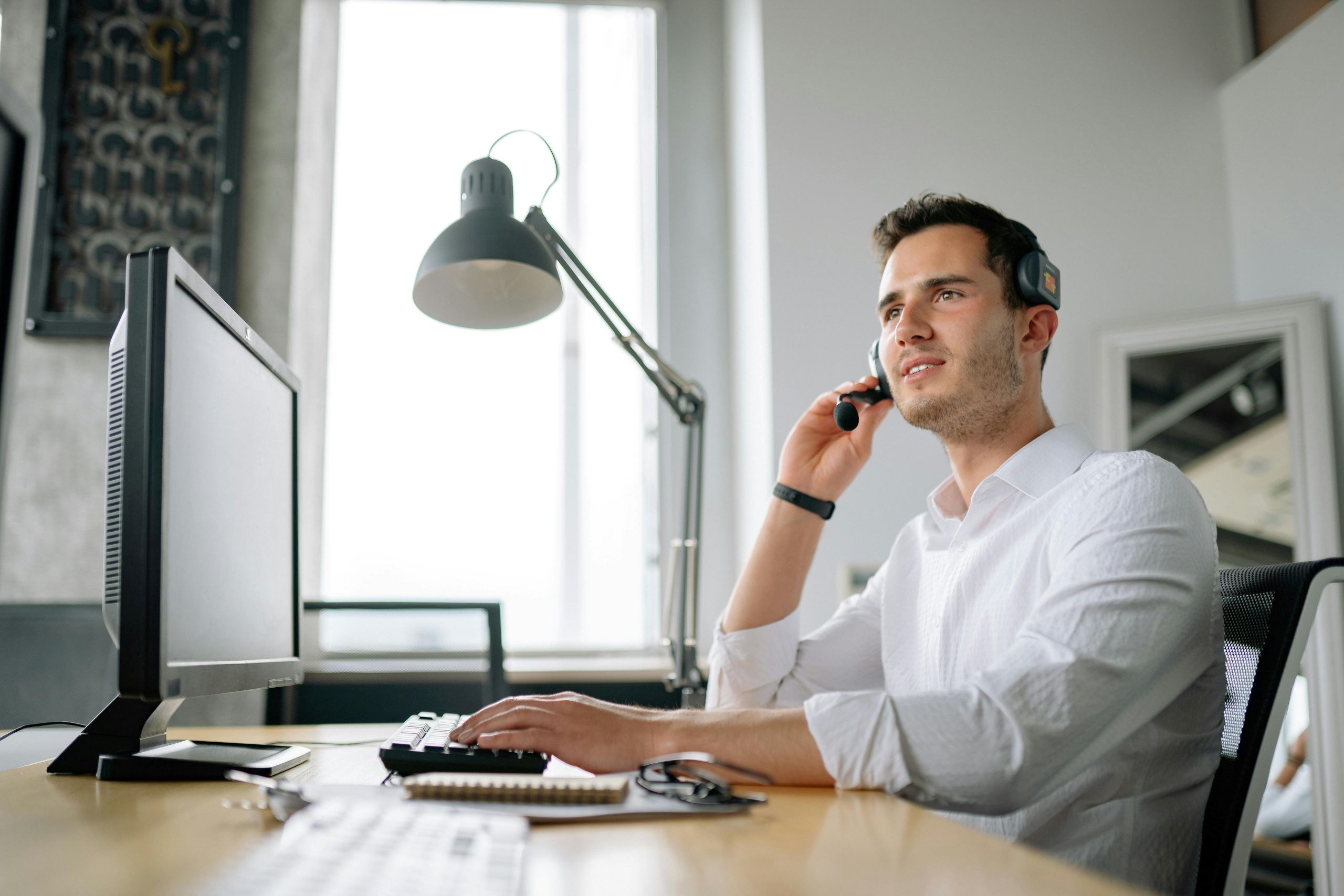 IT support smiling on call wearing headset in front of work station.