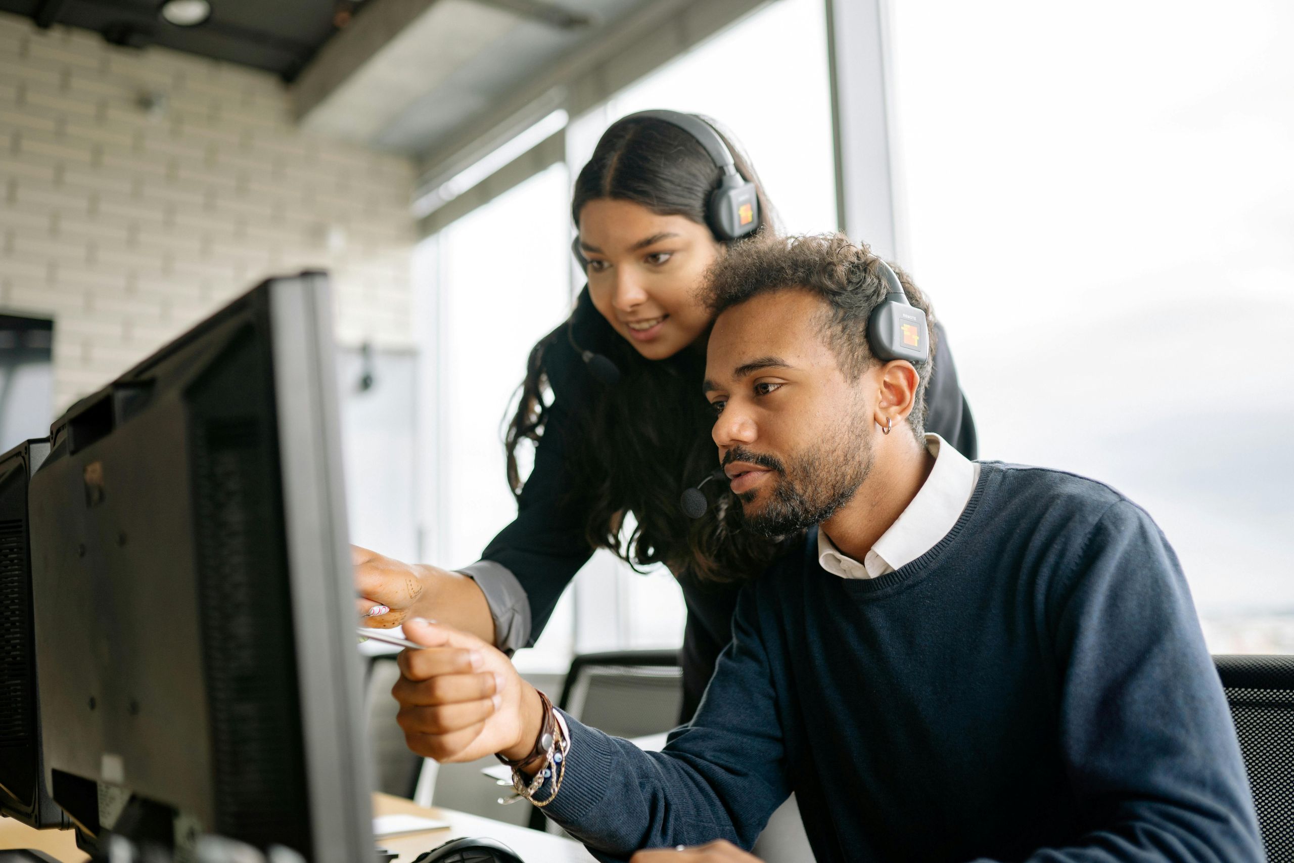 Two coworkers having discussion and pointing at a monitor. Two coworkers having discussion and pointing at a monitor.