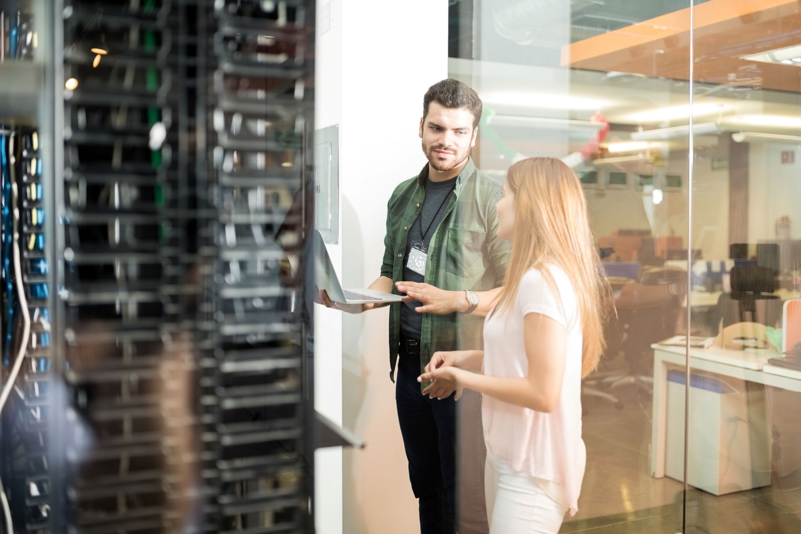 Two people in a server room discussing while holding laptop.